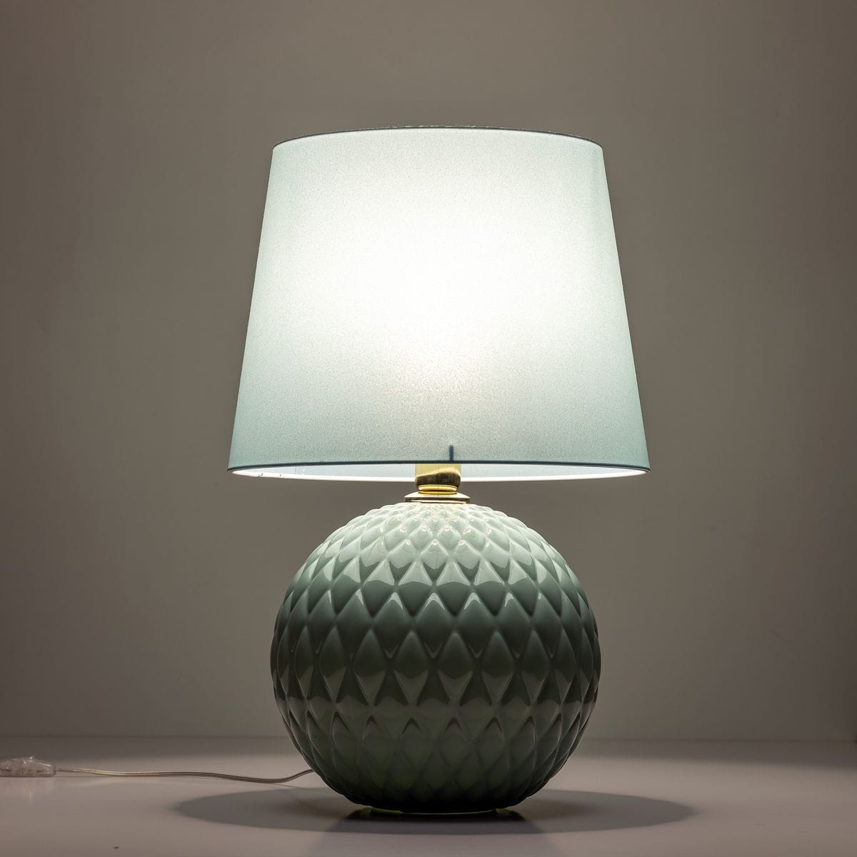 Lampa stołowa Santana w kolorze zielonym/miętowym z okrągłą, teksturowaną podstawą oraz prostym, lekko przezroczystym kloszem. Ujęcie z boku, stojąca na płaskiej powierzchni, z widocznym kablem.