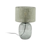 Lampa stołowa Melody z kloszem w kolorze zielonym i podstawą w grafitowym odcieniu. Okrągła, szklana podstawa z lekko przezroczystego materiału, z widocznym kablem. Klosz tekstylny o fakturze, umieszczony na górze.
