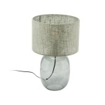 Lampa stołowa Melody z grafitowym, szklanym korpusem i zielonym, tekstylnym kloszem. Ujęcie frontalne, lampa stoi na płaskiej powierzchni, widoczny przewód zasilający. Klosz ma okrągły kształt i delikatną fakturę materiału.