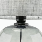Lampa stołowa Melody z grafitowym podstawą i szarym abażurem, zbliżenie na szklaną kulę i czarny element łączący. Abażur wykonany z tekstylnego materiału, widoczne detale struktury.