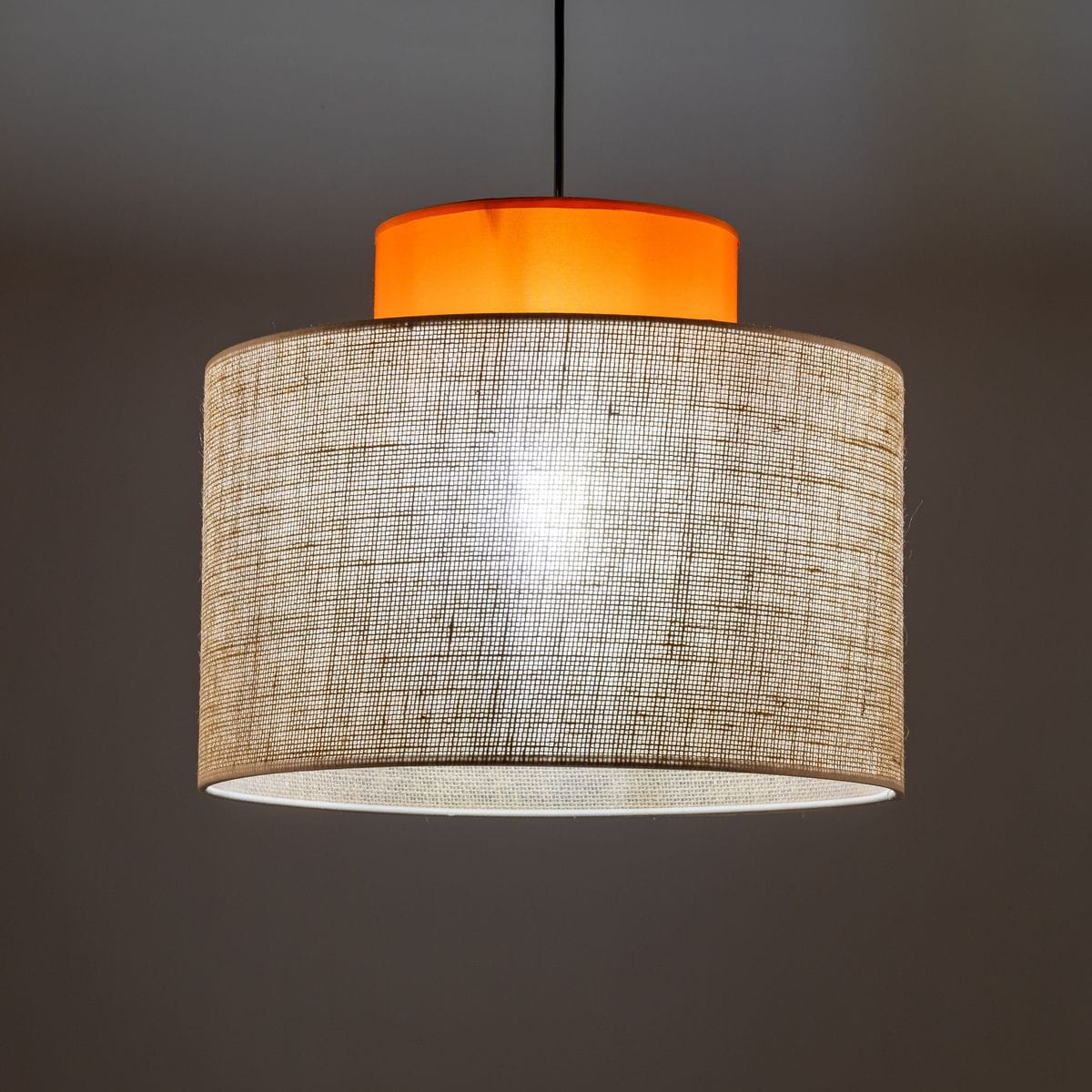 Lampa wisząca Duo D38 z abażurem w kolorze naturalnej juty i pomarańczowym detalem u góry. Okrągły kształt, zawieszona na czarnym przewodzie. Widoczne źródło światła E27. Tło ciemne, podkreślające jasne elementy lampy.