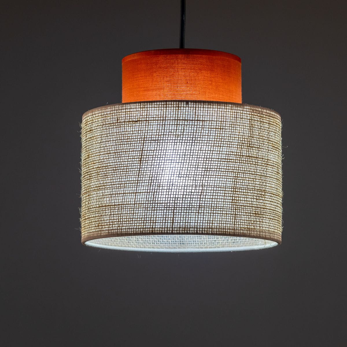 Lampa wisząca Duo D20 z oprawą w kolorze brązowym i kloszem z juty. Kształt cylindryczny, widoczny jeden gwint E27. Ułożona pionowo, z górnym elementem w intensywnym pomarańczowym kolorze. Tło ciemne, co podkreśla detale lampy.