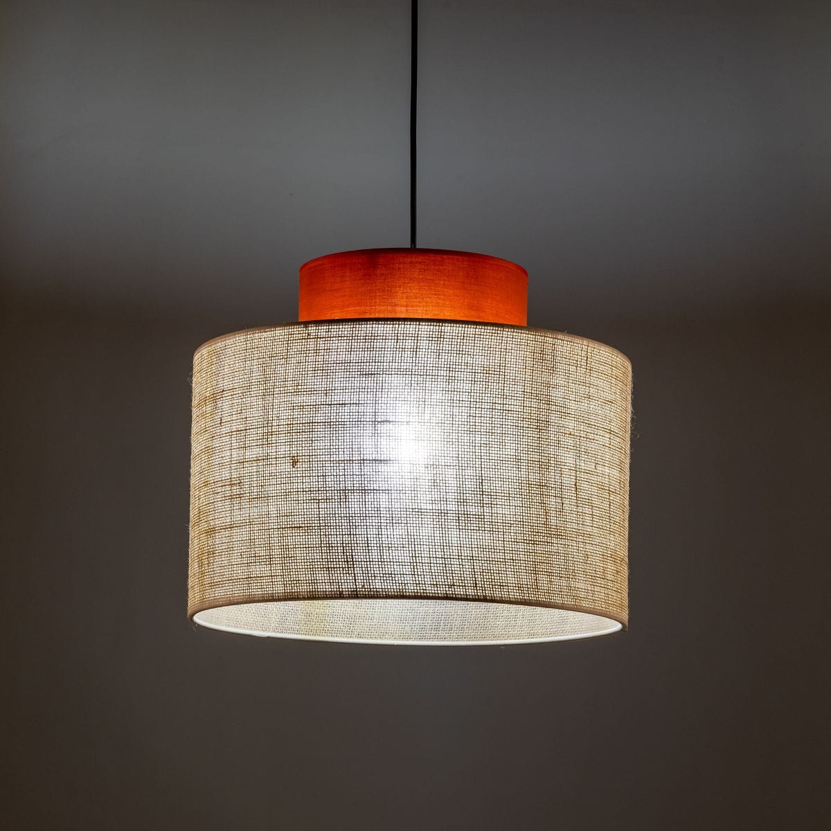 Lampa wisząca Duo D38 z brązowym abażurem z juty i drewnianym elementem u góry. Kształt cylindryczny, zawieszona na cienkim przewodzie, emituje miękkie światło. Tło neutralne, co podkreśla prostotę designu.