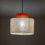 Lampa wisząca Duo D38 z brązowym abażurem z juty i drewnianym elementem u góry. Kształt cylindryczny, zawieszona na cienkim przewodzie, emituje miękkie światło. Tło neutralne, co podkreśla prostotę designu.