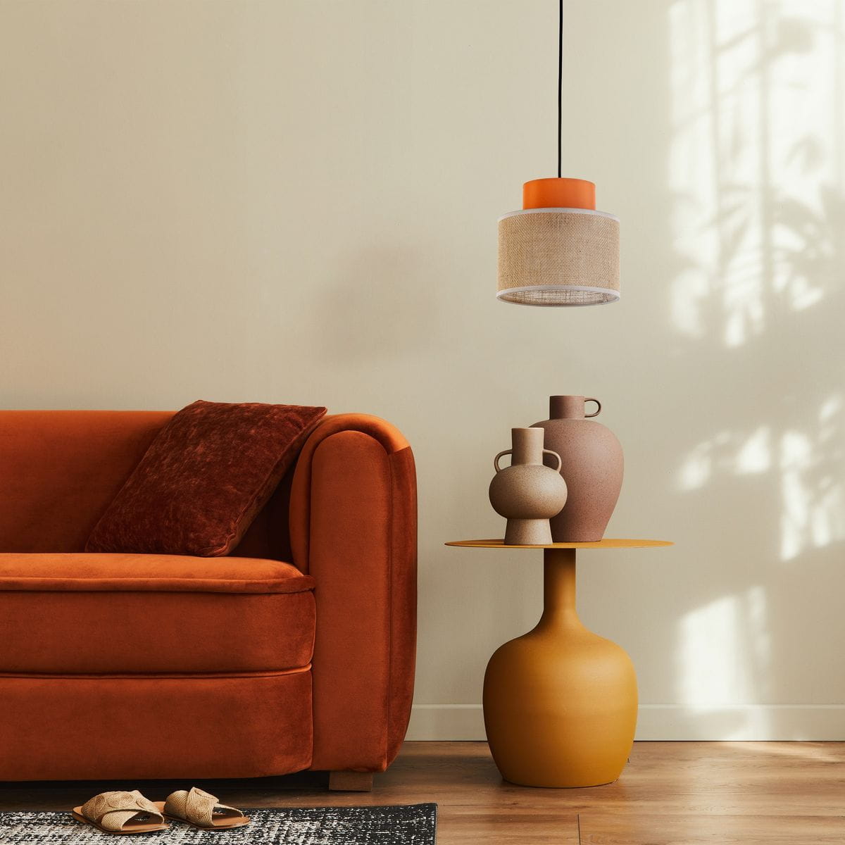 Lampa wisząca Duo D20 z kloszem w kolorze pomarańczowym i jutowym, zawieszona nad stolikiem z ceramiką, w otoczeniu pomarańczowej sofy. Widoczny czarny przewód oraz subtelne cienie na ścianie.