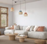 Duo lampa wisząca 3xE27 w kolorach pomarańczowym, niebieskim i naturalnym z juty. Zawieszona na czarnych kablach w nowoczesnym wnętrzu, nad kanapą z poduszkami, w otoczeniu drewnianych stolików.