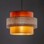 Lampa wisząca Trio z jedną oprawą E27, składająca się z trzech okrągłych kloszy w kolorach pomarańczowym, żółtym i szarym, z teksturowanym elementem z tkaniny. Wisi na czarnym kablu, prezentując nowoczesny design.