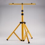 Przenośny statyw naświetlacza LED, wykonany z żółtego metalu, z regulowaną wysokością. Posiada trzy stabilne nogi i górny uchwyt do zamocowania lampy. Tło jasnoszare, co podkreśla konstrukcję statywu.