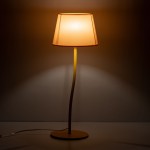 Lampka stołowa Nicola z kloszem w kolorze żółtym, z prostą, zakrzywioną podstawą i widocznym kablem. Klosz ma formę stożka, emitując ciepłe światło, ustawiona na białym tle.