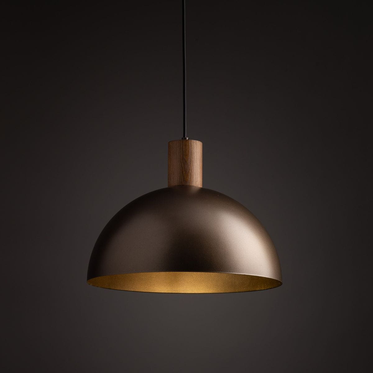 Lampa wisząca Oslo z brązowym kloszem z metalu, z drewnianym uchwytem. Klosz w kształcie półkuli z matowym wykończeniem, wewnątrz złota. Zawieszona na czarnym przewodzie, prezentująca nowoczesny design.