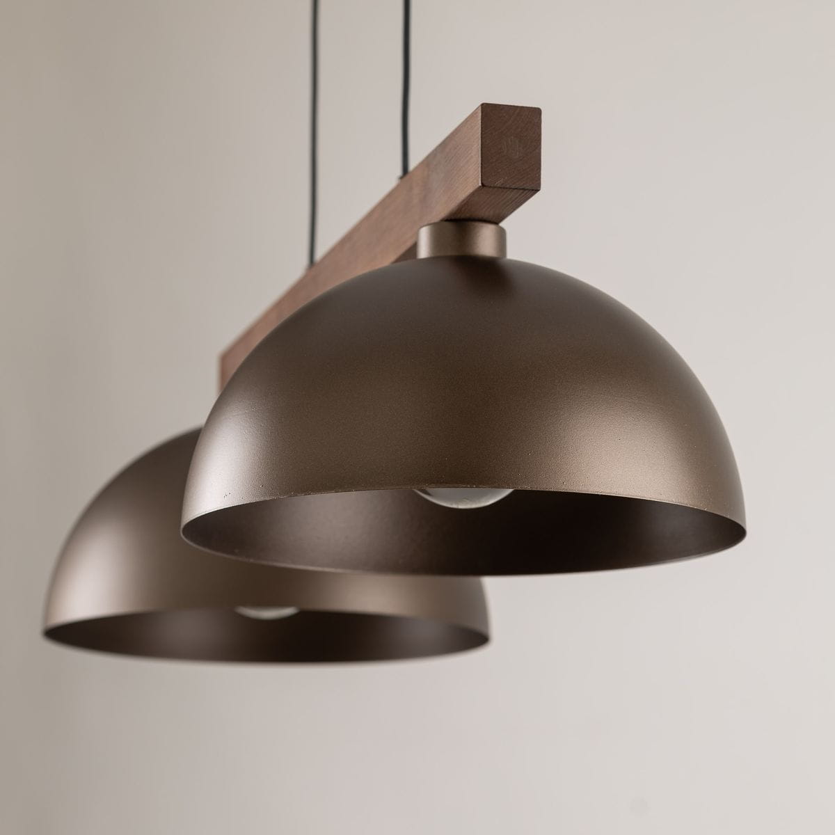 Lampa wisząca Oslo z dwoma kloszami w kolorze brązowym, wykonana z metalu, zawieszona na drewnianym elemencie. Widoczne dwa okrągłe klosze o matowej powierzchni, zawieszone na czarnych przewodach. Tło jasne, minimalistyczne.