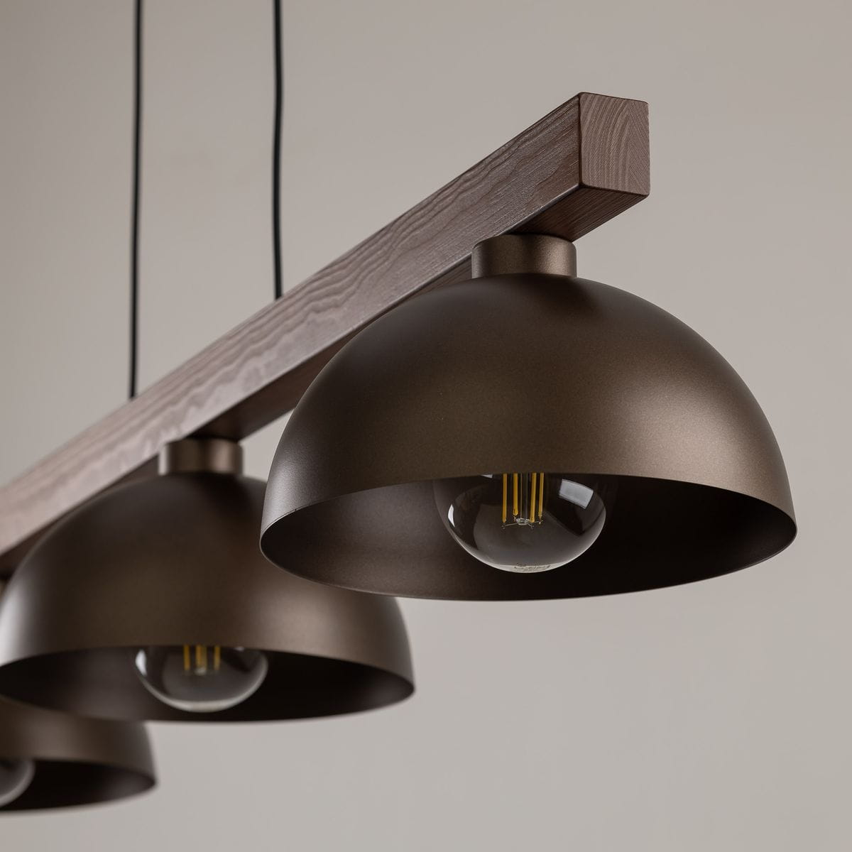 Lampa wisząca Oslo z trzema kloszami E27 w kolorze brązowym, z drewnianym wspornikiem. Klosze mają zaokrąglony kształt i matowe wykończenie. Produkt zawieszony na czarnych przewodach, idealny do nowoczesnych wnętrz.