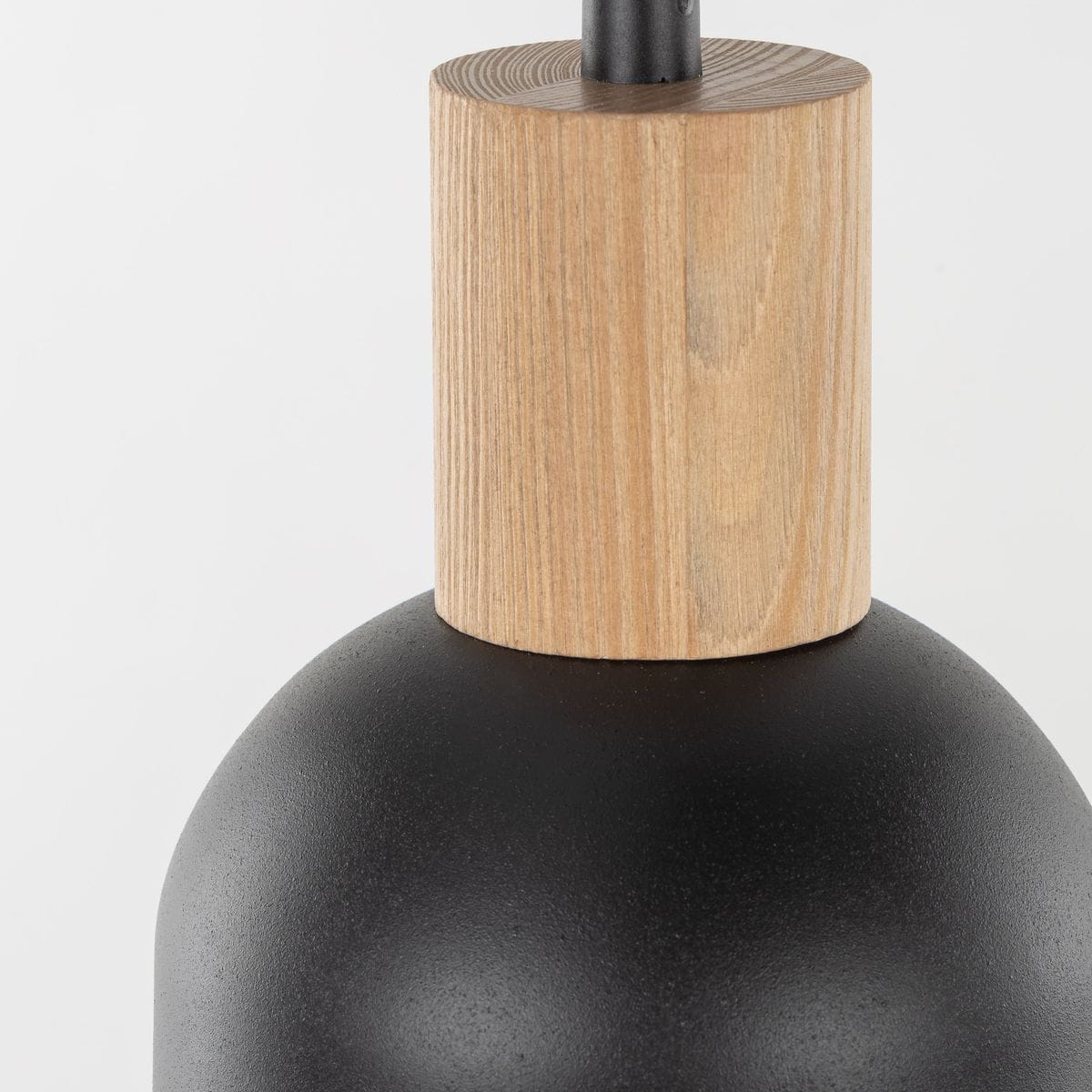 Lampa wisząca Cairo z trzema oprawami E27, w czarnym kolorze. Górna część wykonana z drewna, z widocznym słoje. Kształt zaokrąglony, matowa powierzchnia. Ujęcie z bliska, eksponujące detal połączenia materiałów.