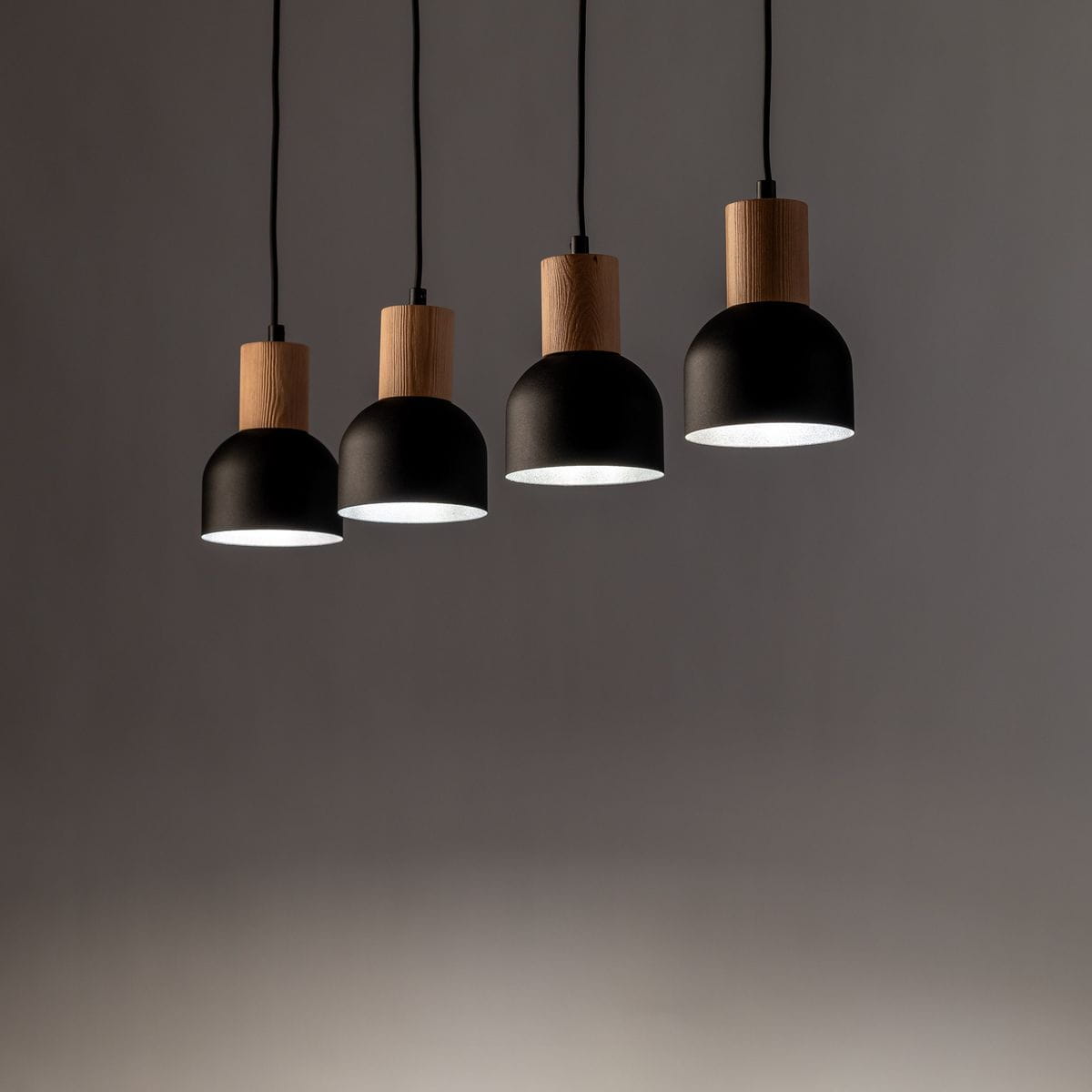 Cairo lampa wisząca z czterema kloszami, czarna, z drewnianymi elementami, zawieszona na czarnych przewodach. Klosze mają okrągły kształt i matowe wykończenie, emitują ciepłe światło. Ujęcie z przodu, na szarym tle.