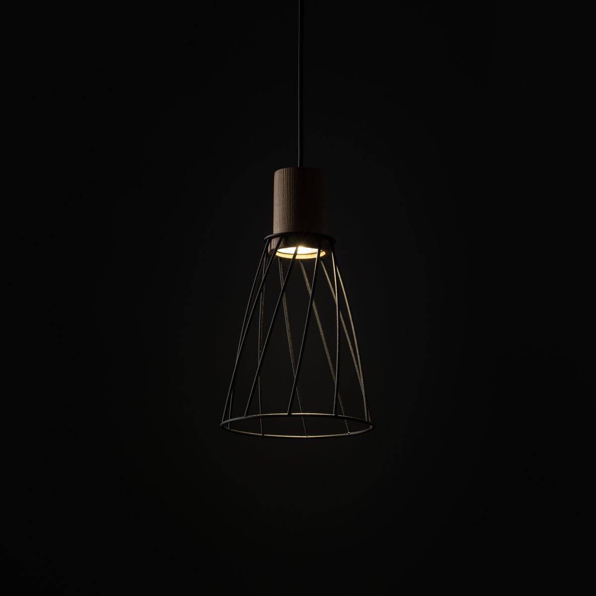 Lampa wisząca Modesto D16 z czarnym metalowym kloszem w kształcie stożka oraz jasnym drewnianym uchwytem. Ujęcie z boku, na ciemnym tle, pokazujące źródło światła GU10 wewnątrz klosza.