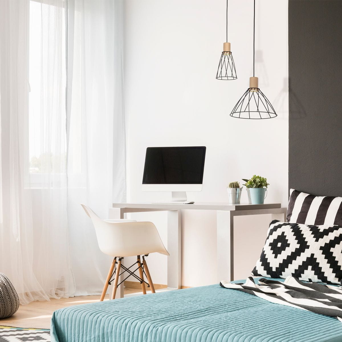 Czarna lampa wisząca Modesto D16 z kloszem w kształcie stożka, wykonana z metalu, zawieszona na cienkim przewodzie. W tle nowoczesne biurko z komputerem i rośliną, w jasnym wnętrzu z delikatnymi zasłonami.