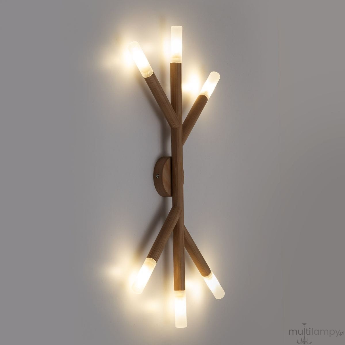 Lampa sufitowa Noble w jasnym drewnie z sześcioma źródłami światła G9. Kształt przypominający gałęzie, zamontowana na ścianie, emitująca ciepłe, rozproszone światło. Transparentne klosze na końcach ramion, które dodają nowoczesnego charakteru.