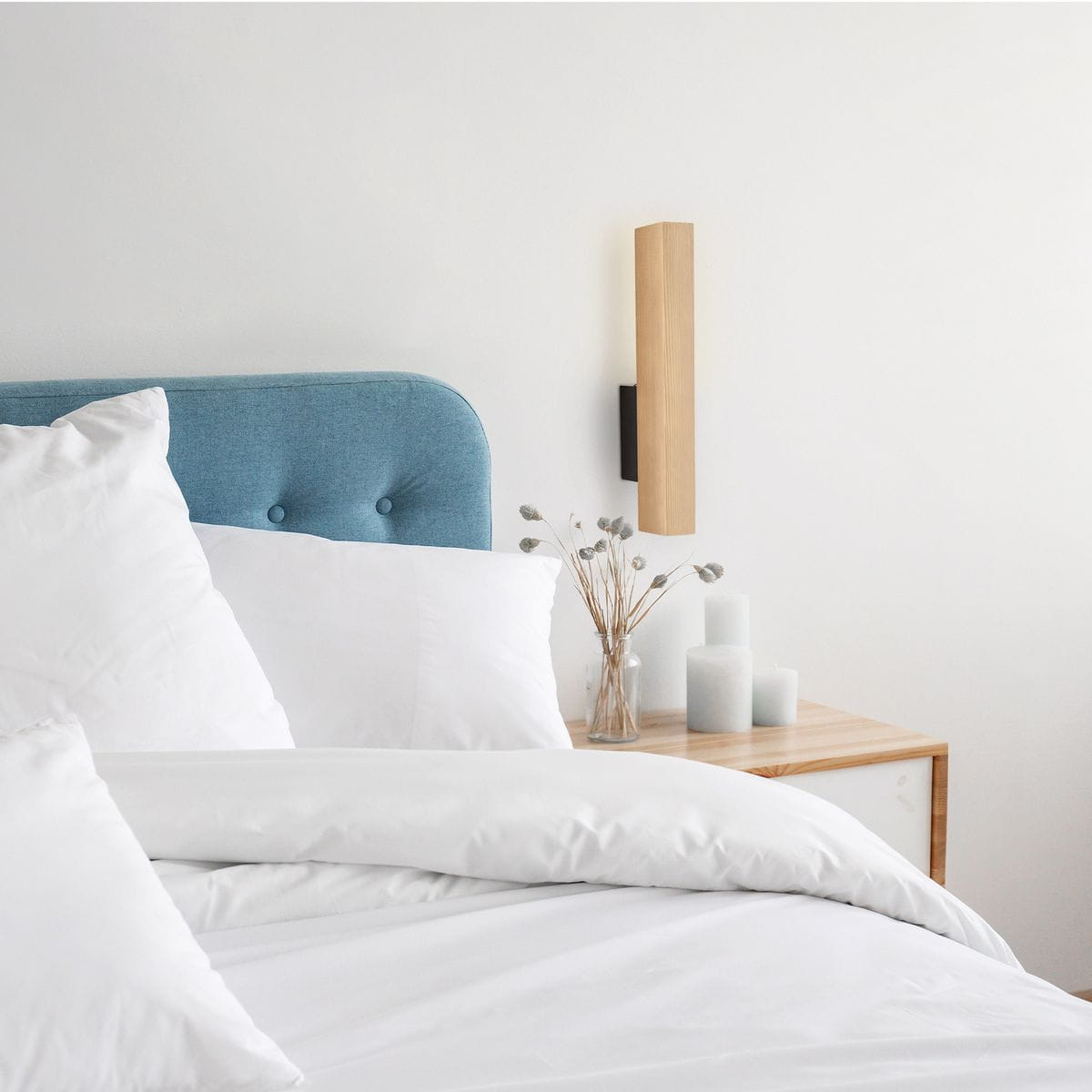 Kinkiet Teo 1xLED/3W w kolorze czarnym z jasnym drewnem, zamontowany na ścianie obok łóżka. Produkt ma prostokątny kształt i minimalistyczny design, w otoczeniu białej pościeli oraz dekoracyjnych świec w szklanym wazonie.