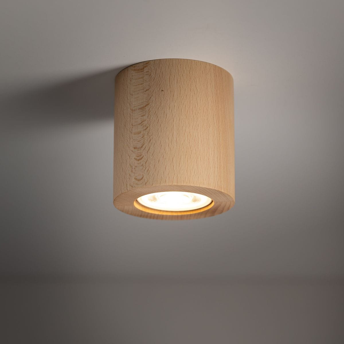 Lampa sufitowa Eve z jasnego drewna, cylindryczna, z oprawą na żarówkę GU10. Ujęcie z dołu, pokazujące wnętrze lampy oraz źródło światła. Neutralne tło podkreśla naturalny charakter materiału.