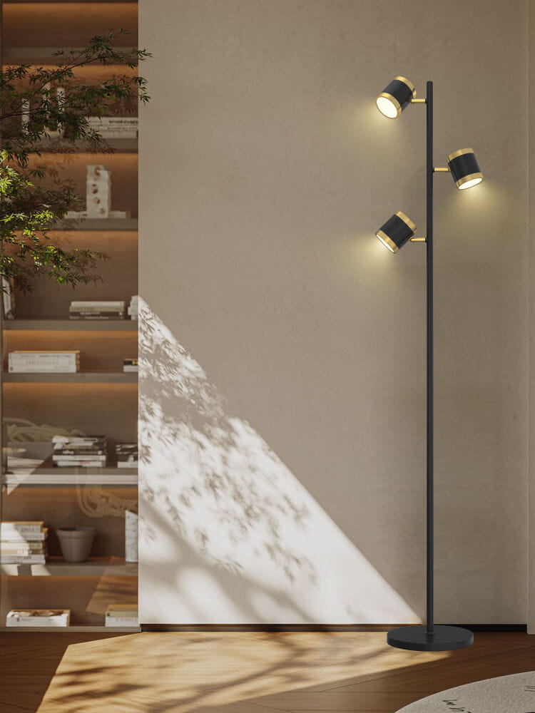 Lampa podłogowa Toulouse w kolorze czarnym i złotym z trzema źródłami światła LED, stojąca na okrągłej podstawie. Ujęcie frontalne, w tle widoczna półka z książkami.