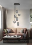 Lampa wisząca Belleville 6xE14 w kolorze czarnym i złotym z sześcioma szklanymi kloszami w odcieniu szarości, zawieszona na długich linkach. Umieszczona w nowoczesnym wnętrzu, nad sofą z poduszkami, w jasnym pomieszczeniu z zasłonami.