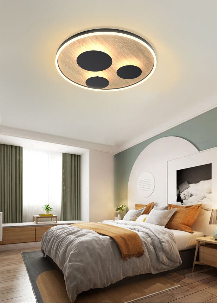Plafon Dijon D60 z czarnym wykończeniem i drewnianym akcentem, montowany na suficie. Okrągły kształt z trzema ciemnymi okręgami i podświetleniem LED, idealny do nowoczesnych wnętrz. Widok z góry, umieszczony w sypialni z jasnymi zasłonami.