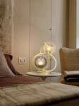 Lampa stołowa Metz 2xG9 w kolorze złotym, z dekoracyjną oprawą w kształcie spirali, umieszczona na białym stoliku obok łóżka. W tle widoczne jasne ściany oraz tekstylia w stonowanych kolorach.