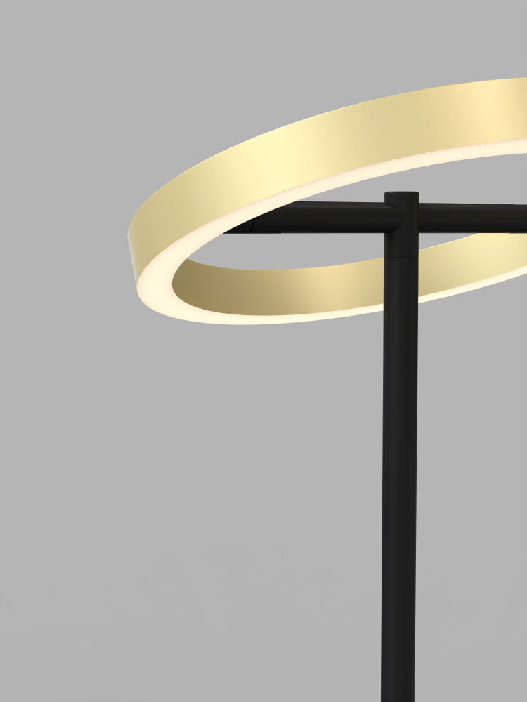 Lampa stołowa Brest z czarnym stelażem i złotym pierścieniem LED. Kąt ujęcia z boku, ukazujący detal złotego klosza i prostą, nowoczesną formę. Tło w odcieniach szarości, podkreślające elegancję lampy.