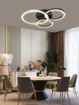 Lampa sufitowa Bayeux z trzema pierścieniami LED w kolorze czarnym i złotym. Ułożona na suficie, tworzy nowoczesny akcent w aranżacji. Widoczna w eleganckim wnętrzu z okrągłym stołem i krzesłami, z dekoracyjnymi elementami w tle.