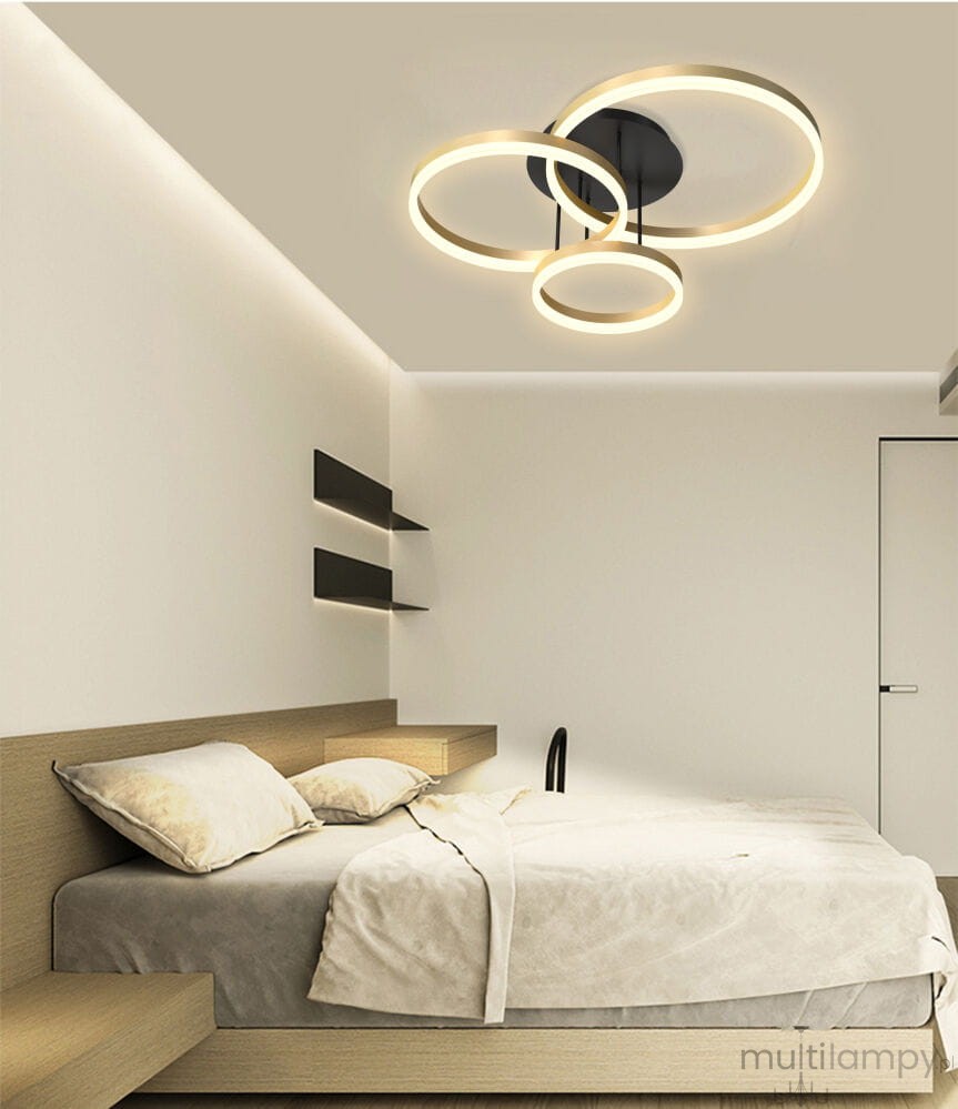 Lampa sufitowa Perpignon z trzema okrągłymi źródłami LED w kolorze czarnym i złotym, zamontowana na suficie. Widok z dołu, w nowoczesnej sypialni z jasnymi ścianami i minimalistycznym wystrojem.