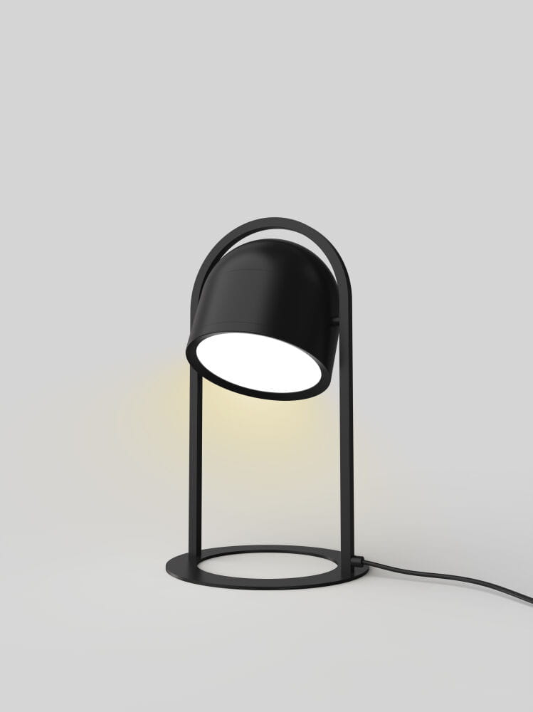 Czarna lampa stołowa Nizza z jedną żarówką LED 10,5W, z okrągłą podstawą i półkolistym kloszem, ustawiona na szarym tle. Klosz jest lekko nachylony, co podkreśla nowoczesny design lampy. Widoczny przewód zasilający.
