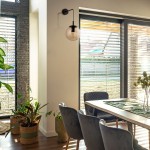 Kinkiet Esme 1xE27 w kolorze czarnym z topazową, szklaną kloszową kulą, zamontowany na ścianie w jasnym wnętrzu. W tle widoczne okna z żaluzjami oraz rośliny doniczkowe. Oświetlenie w estetycznym kontekście domowym.