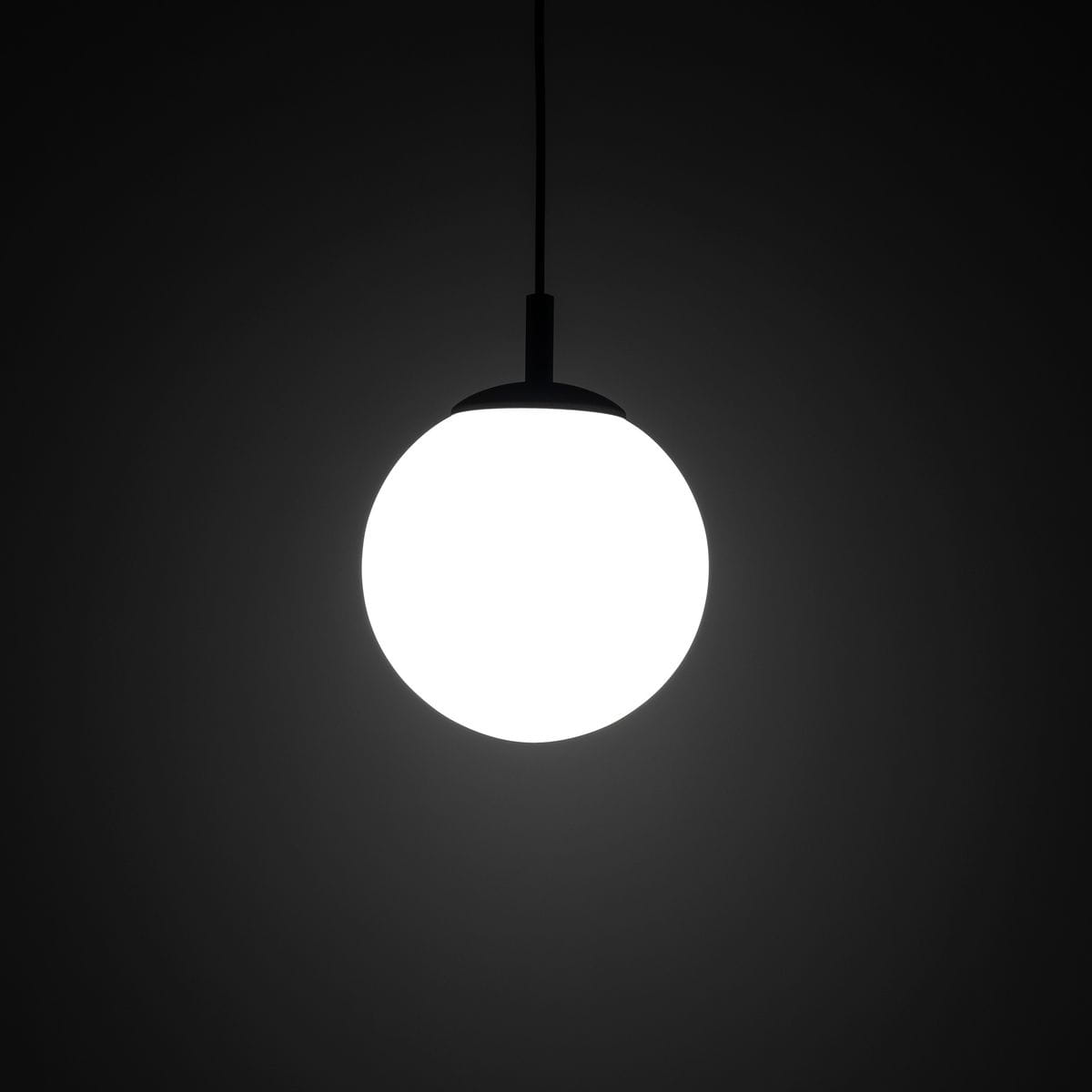 Lampa wisząca Esme D25 z okrągłym, białym kloszem oraz czarnym mocowaniem. Produkt zawieszony na cienkim przewodzie, na jednolitym ciemnym tle. Idealna do nowoczesnych aranżacji wnętrz. Wymaga żarówki E27.