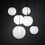 Lampa wisząca Esme z sześcioma okrągłymi kloszami w kolorze białym, zawieszona na cienkich czarnych przewodach. Klosze mają matową powierzchnię i różne rozmiary, tworząc efektowną kompozycję. Tło jest ciemne, co podkreśla jasność lampy.
