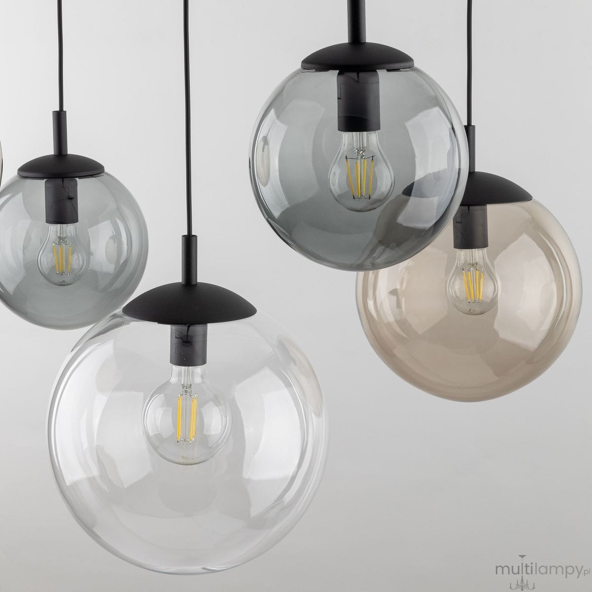 Lampa wisząca Esme z pięcioma kloszami w różnych kolorach (przezroczysty, szary, brązowy) z czarnymi elementami mocującymi. Klosze mają okrągły kształt, a w każdym znajduje się żarówka E27. Produkt zawieszony na cienkich linkach, na jasnym tle.