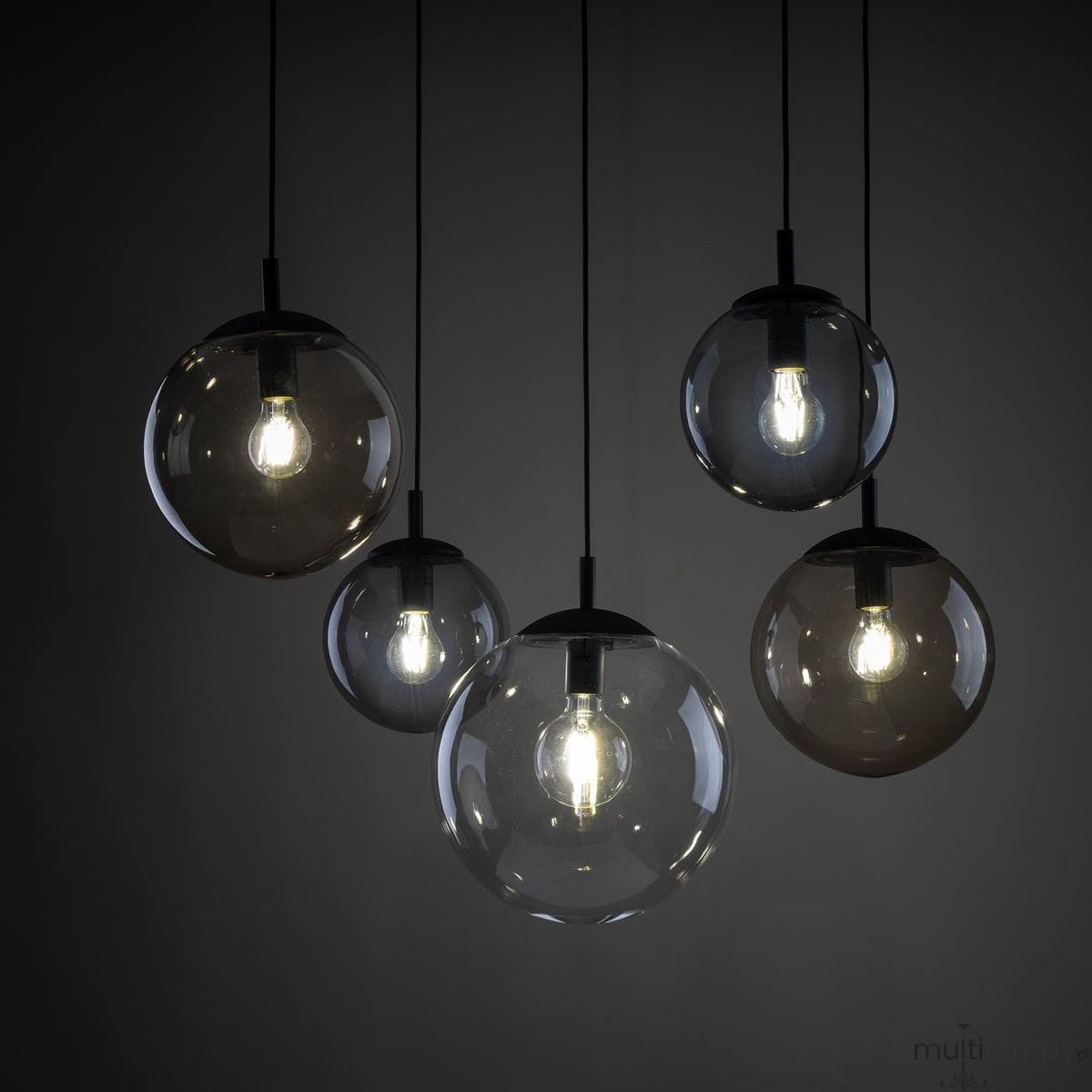 Lampa wisząca Esme z pięcioma kulistymi kloszami w kolorze czarnym i szarym, zawieszona na czarnych przewodach. Klosze wykonane z przezroczystego szkła, z widocznymi żarówkami E27, emitującymi ciepłe światło. Tło ciemne, podkreślające elegancję lampy.