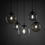 Lampa wisząca Esme z pięcioma kulistymi kloszami w kolorze czarnym i szarym, zawieszona na czarnych przewodach. Klosze wykonane z przezroczystego szkła, z widocznymi żarówkami E27, emitującymi ciepłe światło. Tło ciemne, podkreślające elegancję lampy.