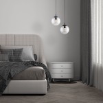 Lampa wisząca Esme D30 z jedną oprawą E27, czarna i transparentna. Dwa okrągłe klosze zawieszone na czarnych przewodach. Lampa umieszczona nad łóżkiem w nowoczesnej sypialni z szarym kocem i białą komodą.