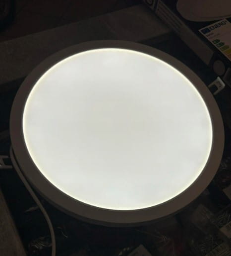 Panel LED D30 8w1/12-24W/3-4-6000K, natynkowy podtynkowy, okrągły kształt, biały kolor, z równomiernym źródłem światła. Widoczny z przodu, umieszczony na stole, w otoczeniu akcesoriów elektrycznych.