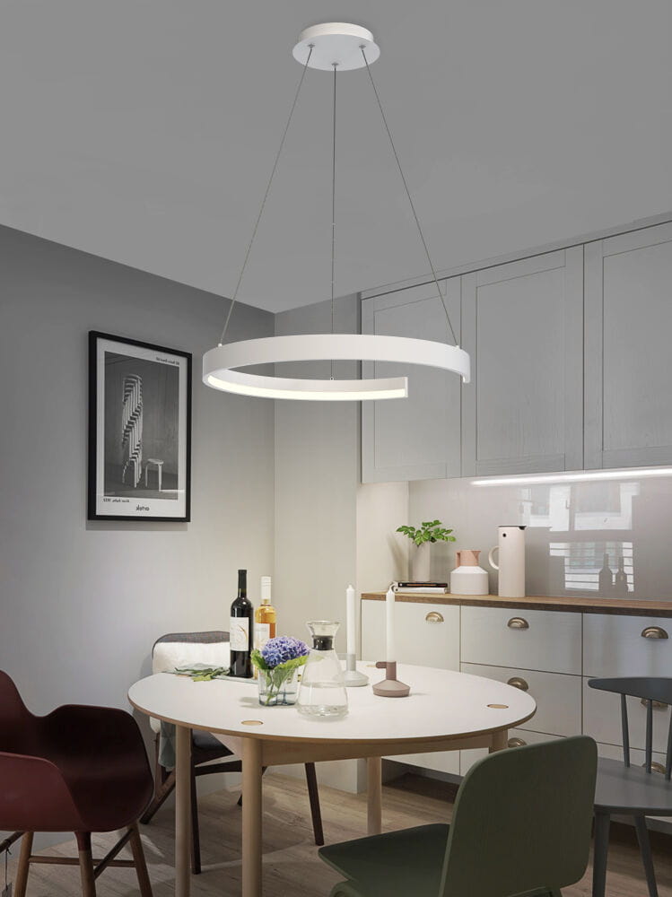Lampa wisząca Fanne 1xLED/34W w kolorze białym, z okrągłym kloszem, zawieszona na cienkich linkach. Umieszczona nad okrągłym stołem w nowoczesnej kuchni, w tle widoczne meble i dekoracje.