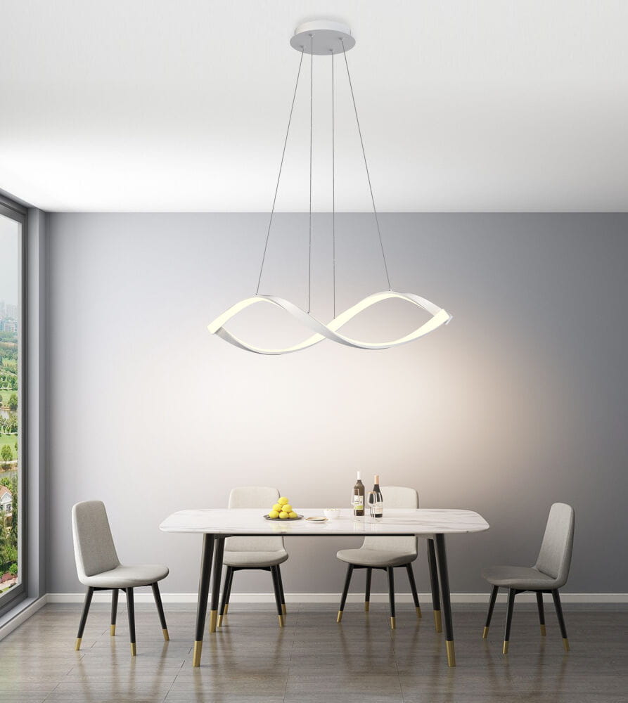 Lampa wisząca Aviano w kolorze białym z jedną diodą LED o mocy 52W, zawieszona na cienkich linkach. Posiada nowoczesny kształt w formie fali, oświetlająca stół w jasnym wnętrzu z szarymi krzesłami i stołem.