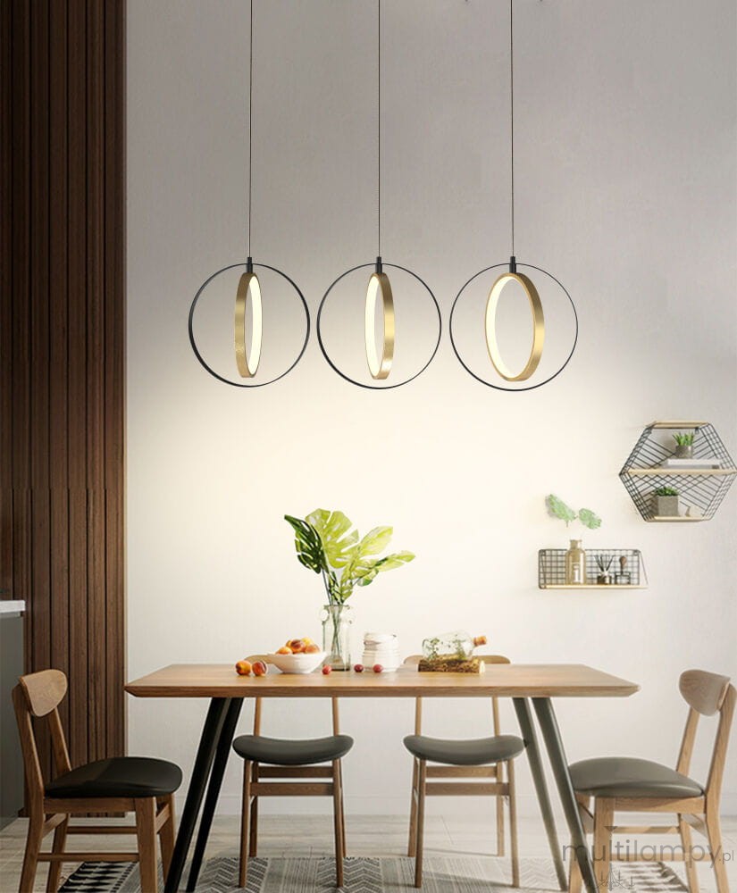 Lampa wisząca Valla 3xLED/24W w kolorze czarnym i złotym, zawieszona na cienkich linkach. Składa się z trzech okrągłych opraw oświetleniowych z metalowymi ramami, umieszczonych nad drewnianym stołem w nowoczesnym wnętrzu.