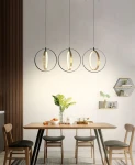 Lampa wisząca Valla 3xLED/24W w kolorze czarnym i złotym, zawieszona na cienkich linkach. Składa się z trzech okrągłych opraw oświetleniowych z metalowymi ramami, umieszczonych nad drewnianym stołem w nowoczesnym wnętrzu.