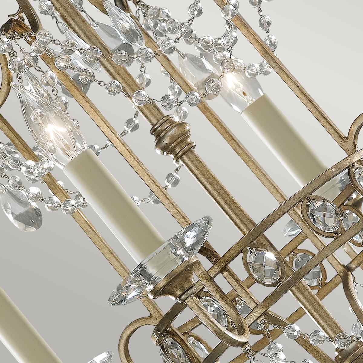 Lampa wisząca Gianna w postarzanym srebrze z czterema gniazdami E14. Widoczne kryształowe elementy dekoracyjne oraz świeczki w białych oprawach. Kąt ujęcia z góry, akcentujący detale i wzory na ramie.