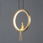 Lampa wisząca Amici w kolorze mosiądzu z okrągłym, złotym ramieniem i LED-owym źródłem światła. Element dekoracyjny w formie siedzącej postaci umieszczony wewnątrz obręczy. Produkt zawieszony na dwóch czarnych linkach, na szarym tle.