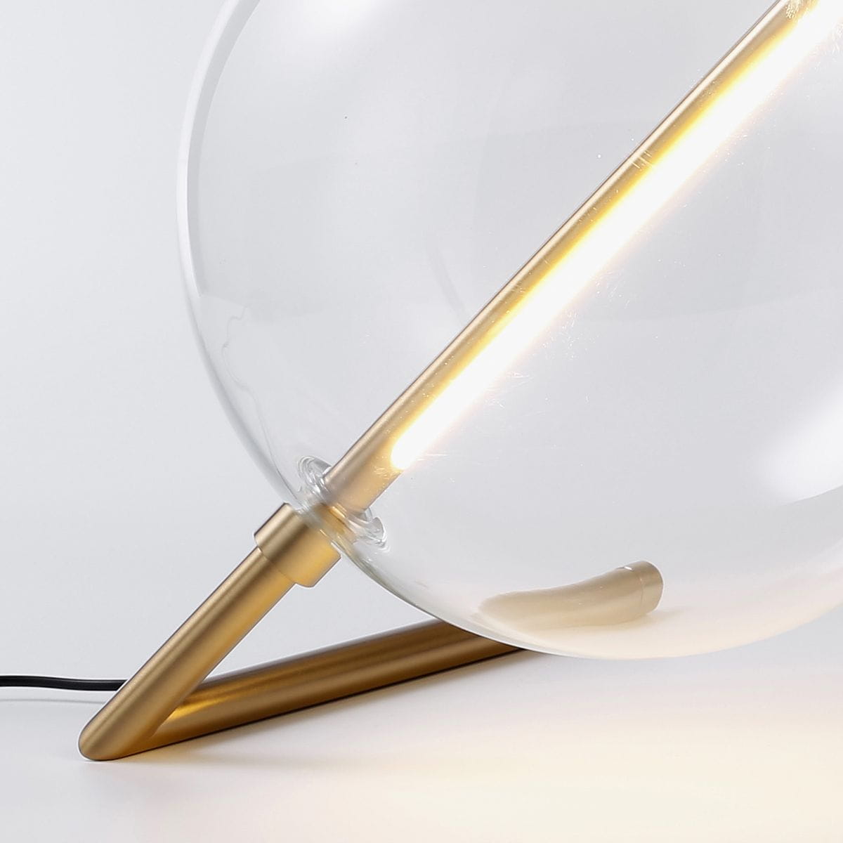 Lampa stołowa Amore z jedną żarówką LED o mocy 12W, z metalową złotą podstawą i szklanym kloszem. Widok z boku, ukazujący delikatny kształt oraz źródło światła w formie pionowej listwy. Tło jasne, minimalistyczne.