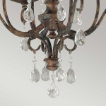 Lampa wisząca Chateau w brązowym, postarzanym wykończeniu z czterema mocowaniami na żarówki E14. Ozdobiona kryształowymi zwisami w kształcie kropli, które dodają elegancji i blasku. Ujęcie z bliska, ukazujące detale konstrukcji.