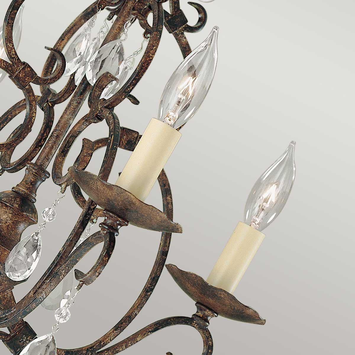 Lampa wisząca Chateau z brązowanego metalu, posiadająca sześć gniazd E14. Ozdobiona kryształowymi elementami i półokrągłymi podstawami na żarówki. Ujęcie z bliska, ukazujące detale mocowania i kształt lampy.