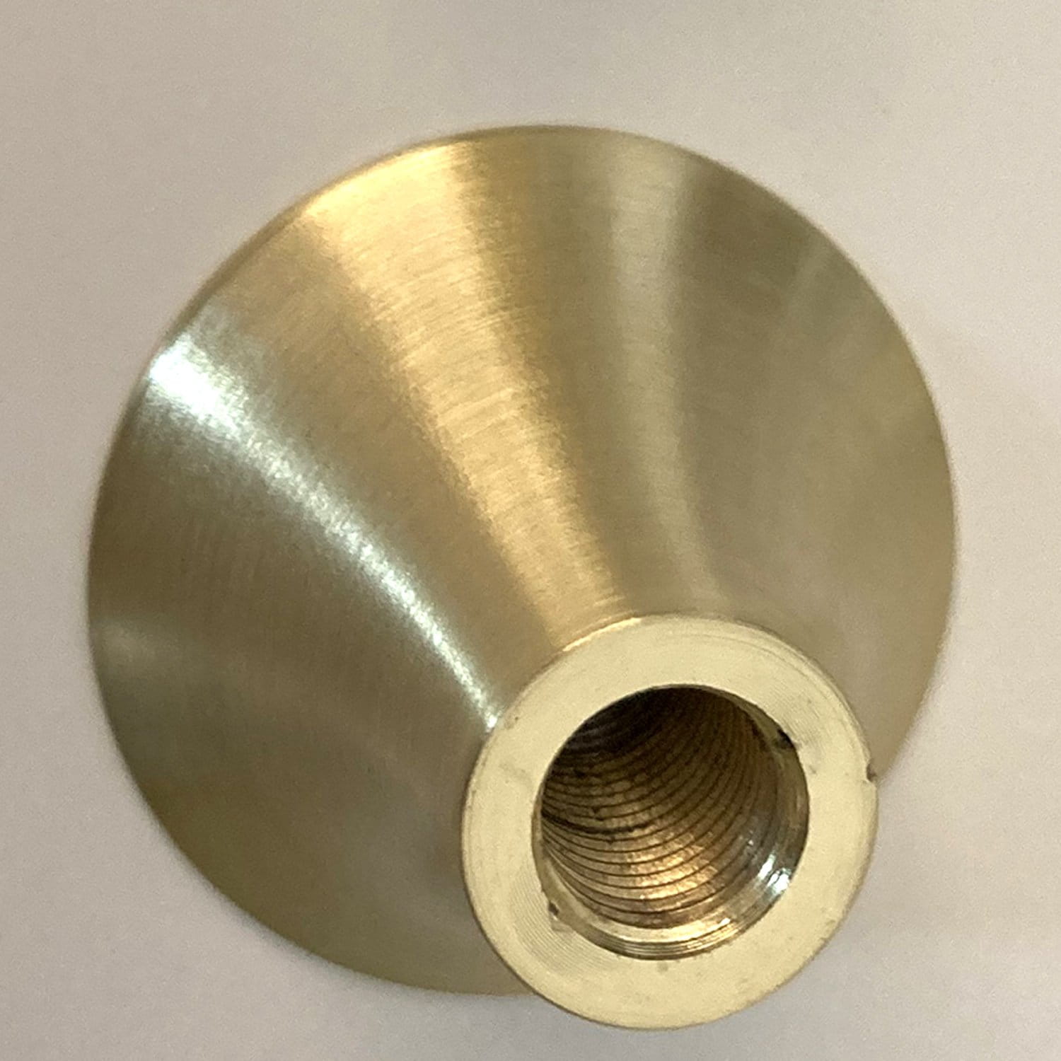 Zbliżenie na metalowy uchwyt lampy wiszącej Artdeco z wykończeniem w złotym szczotkowanym kolorze. Uchwyt ma stożkowy kształt oraz gwint wewnętrzny przystosowany do żarówki E14. Tło proste, białe.