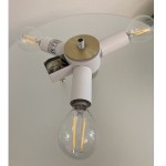 Lampa stołowa Artdeco 3xE14 w kolorze złotym szczotkowanym i białym. Posiada trzy ramiona z oprawkami na żarówki, centralny element w kolorze złotym oraz przezroczyste klosze. Ujęcie z góry, na tle szklanej powierzchni.